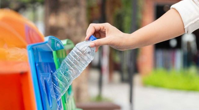 Hand, die Plastikflasche in Recyclingbehälter in öffentlichem Park fallen lässt