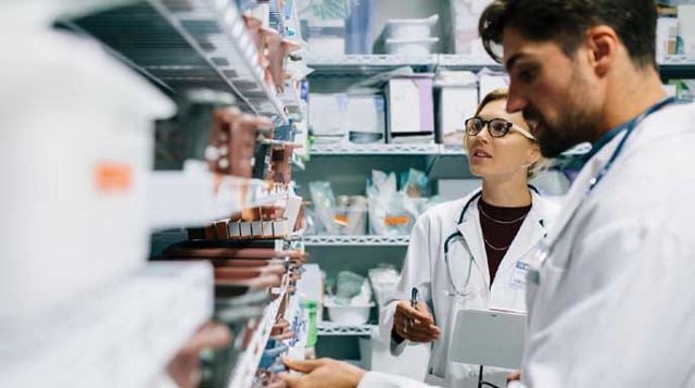 man and woman in lab coats look through shelves of medical supplies