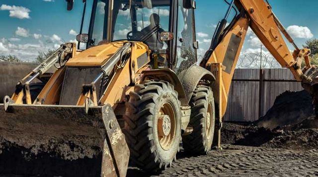 gelber Traktor sammelt Erde mit Eimer