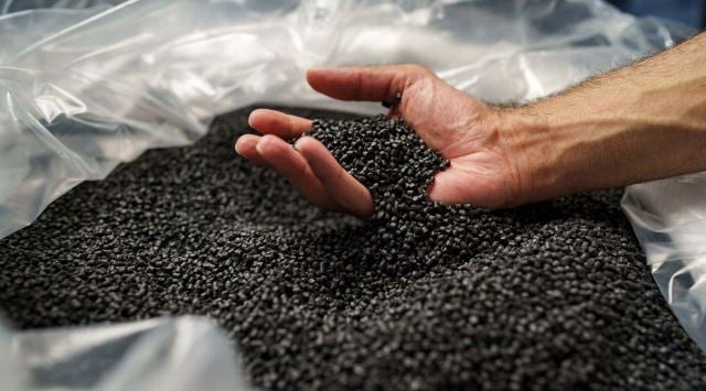 Hand scooping black plastic pellets from bag