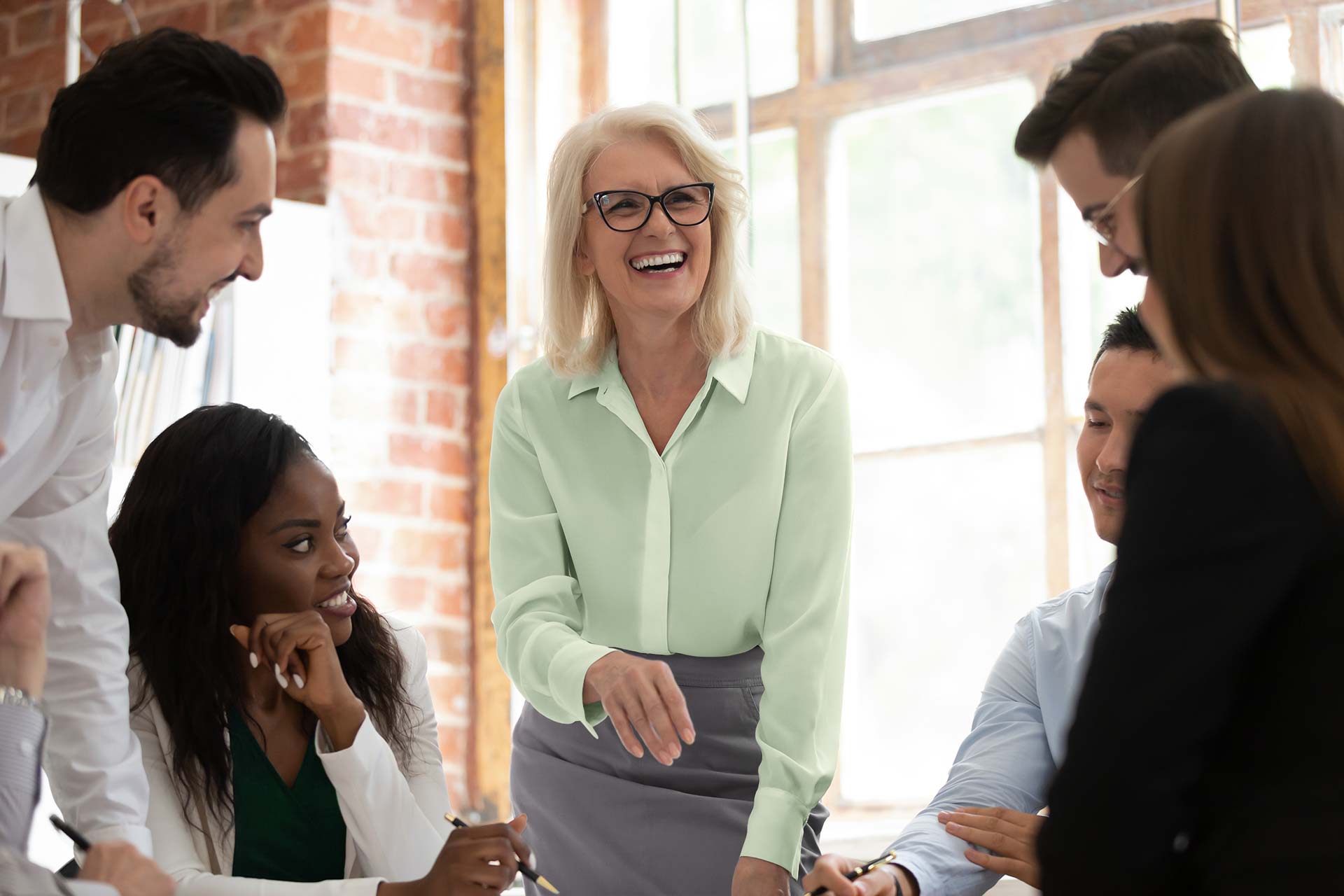 Professional woman standing in center of group of coworkers laughing