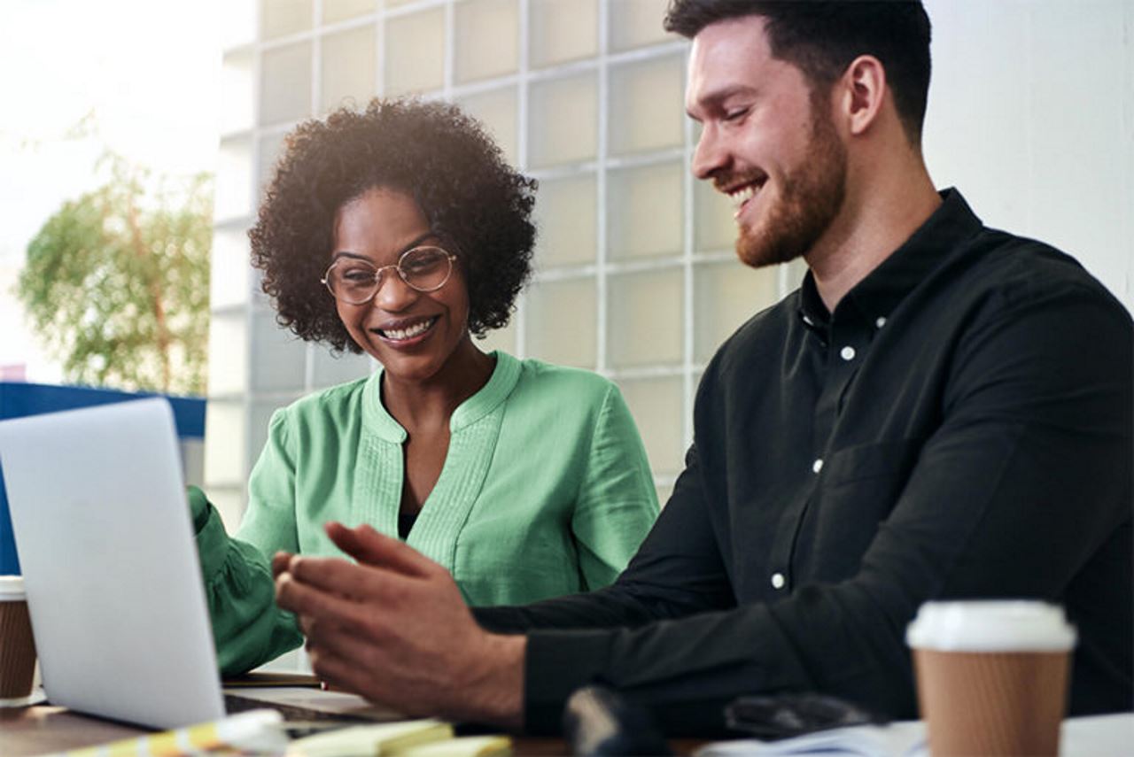 A male and female employee smiling and looking at a laptop screen together