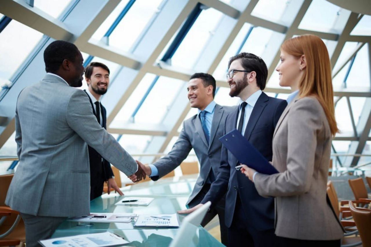 business meeting four men one women shacking hands at table