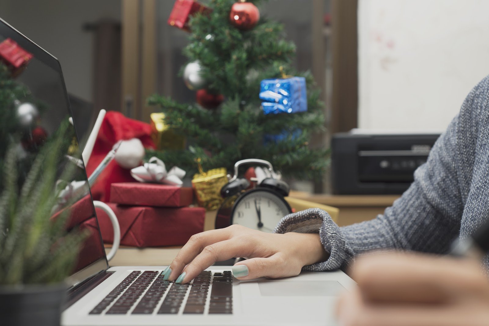 Close-up of person working on a laptop with a christmas tree and presents in the background