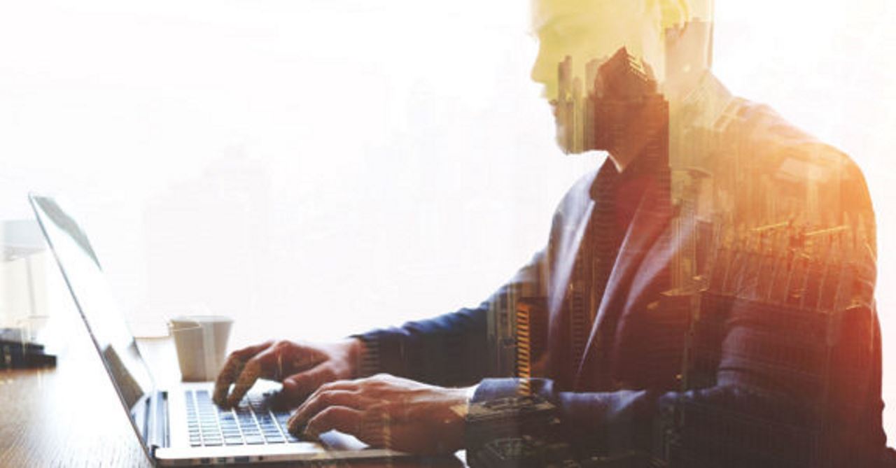 abstract image of a man sitting in front of a laptop with a city image in his silhouette