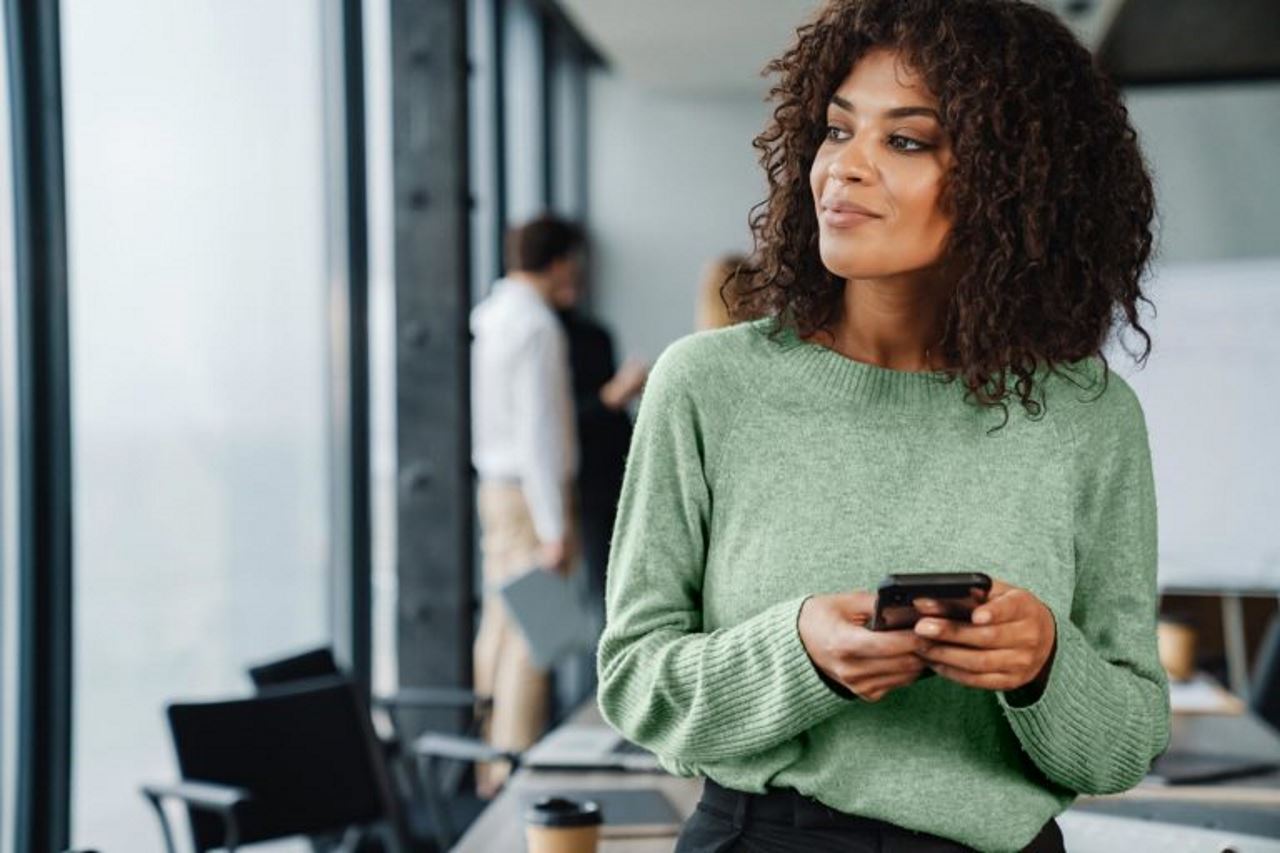 Professional woman in the office, holding her phone and thinking