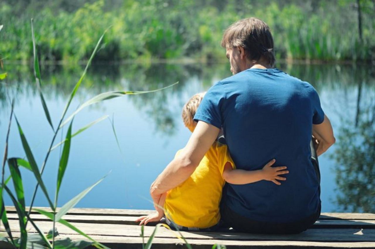 father and young son sitting by a lake