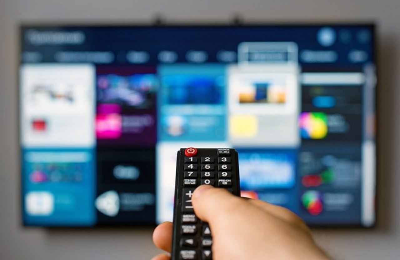 Person holding remote pointing to tv to select netflix