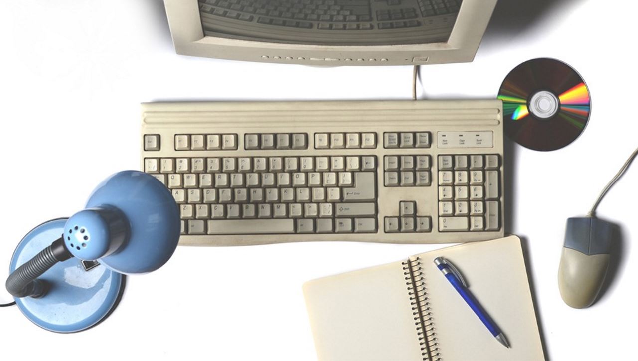 old fashioned computer keyboard and mouse with a CD disk, lamp and notebook