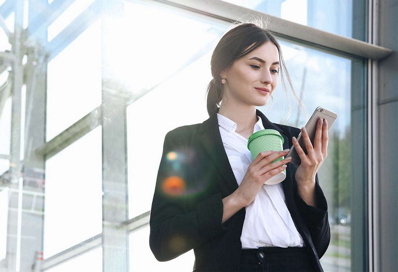 professional woman looking at her phone with a coffee