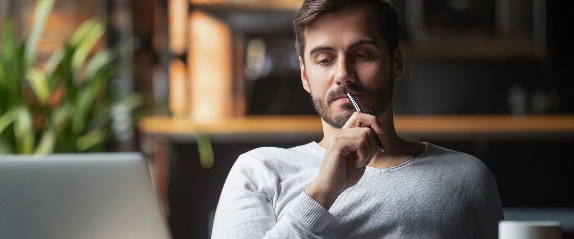 Man thinking holding a pen looking at a laptop screen