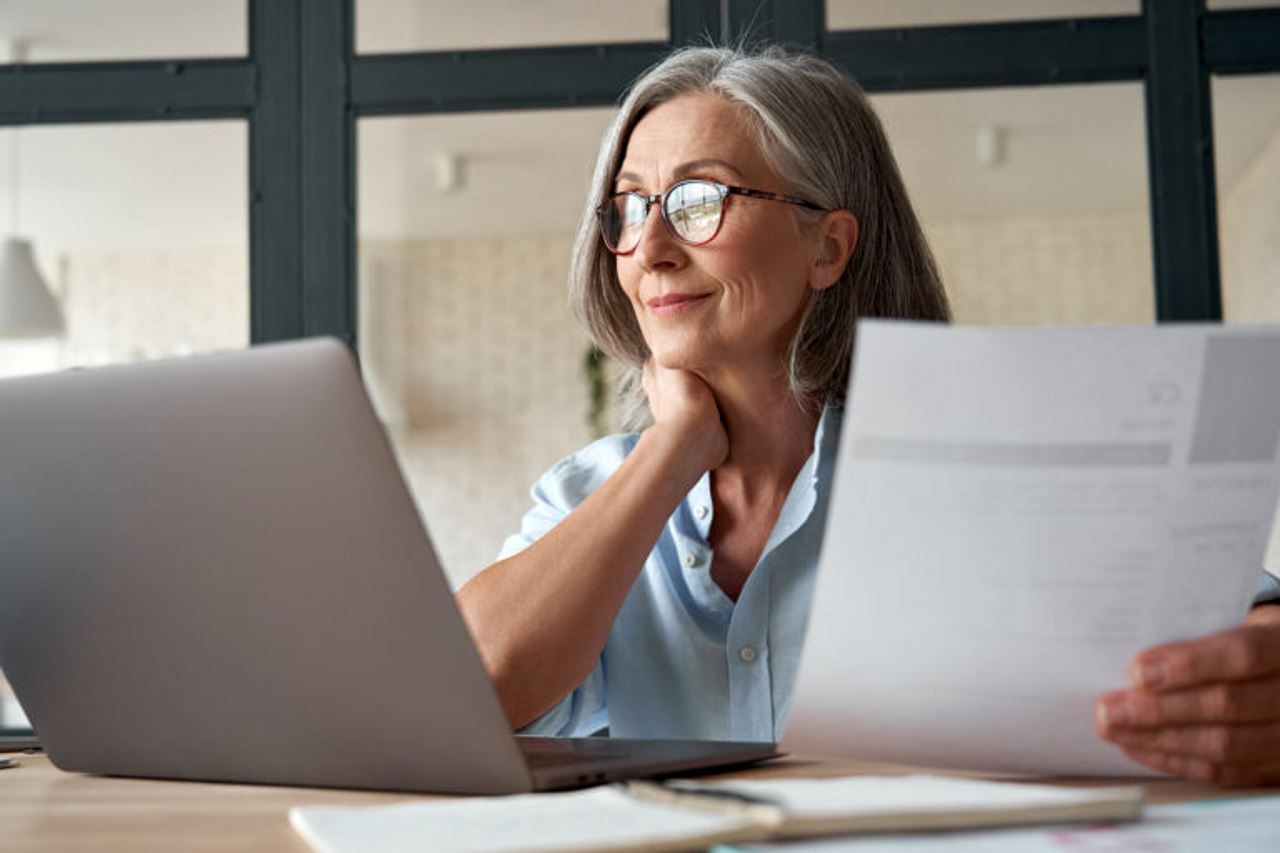 senior woman looking at a laptop screen holding an invoice in her hand