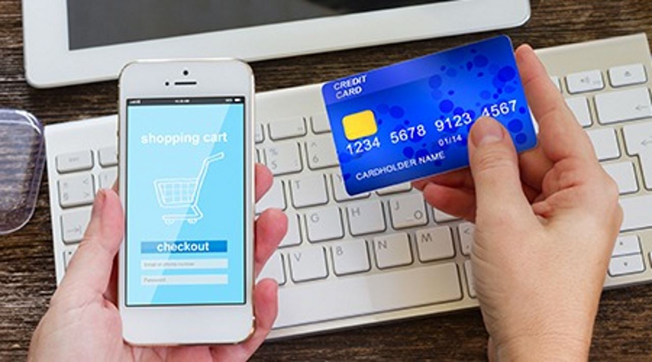 hands holding a phone with a shopping cart screen and a credit card over a keyboard