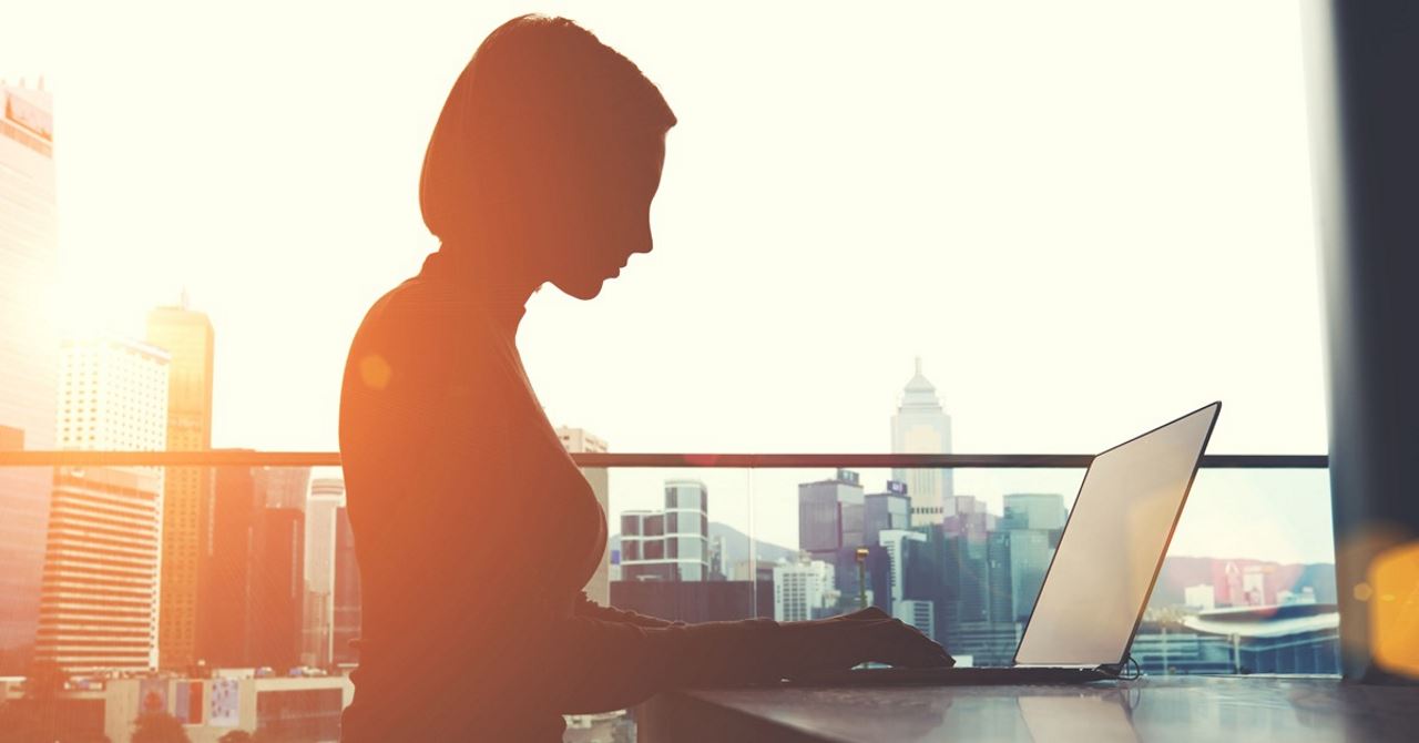 silhouette of woman working on a laptop in an office with a cityscape behind her