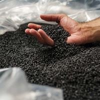 Main ramassant des granulés de plastique noir dans un sac