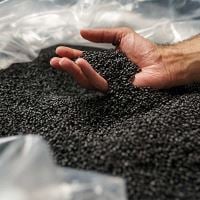 Hand scooping black plastic pellets from bag