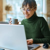 Cliente Billtrust assise devant un ordinateur portable avec une tasse de café pendant un rendez-vous