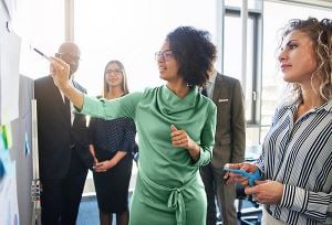 Une femme d'affaires montre un tableau blanc et parle à ses collègues