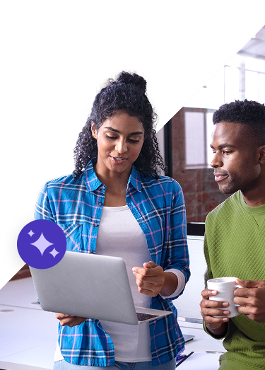 Two people consult a laptop in a work environment. One is holding a coffee while the other explains something