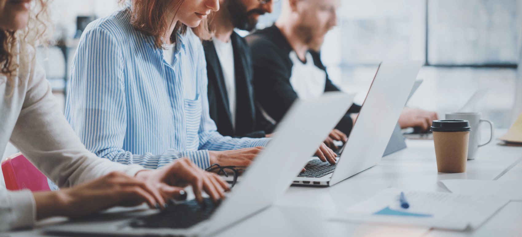 4 versteckte Kosten für Debitorenbuchhaltung technology_employees in einem Büro, das in einer Reihe sitzt und an seinen Laptops arbeitet