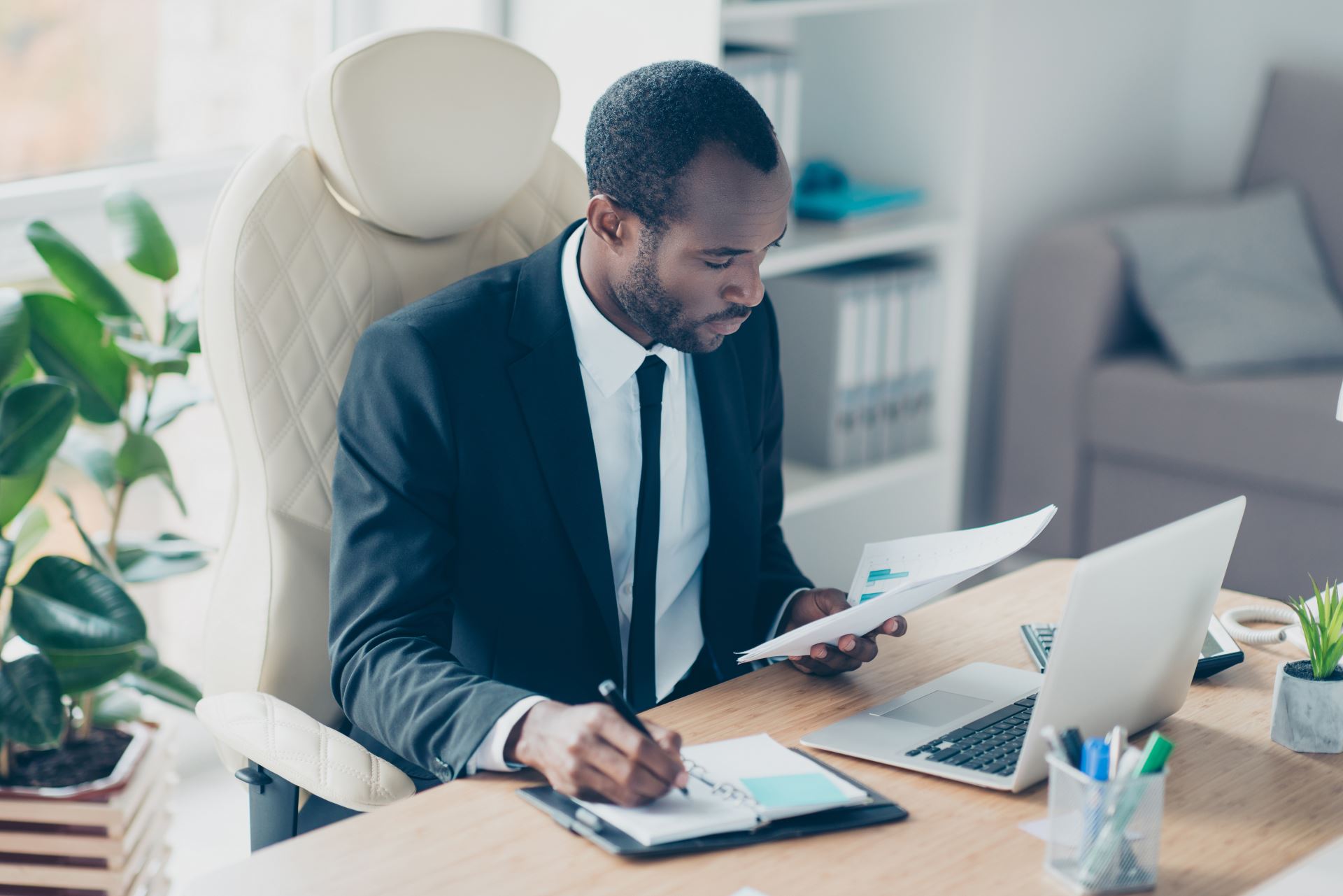 a man in an office at his desk looking at paper and a computer while writing down notes