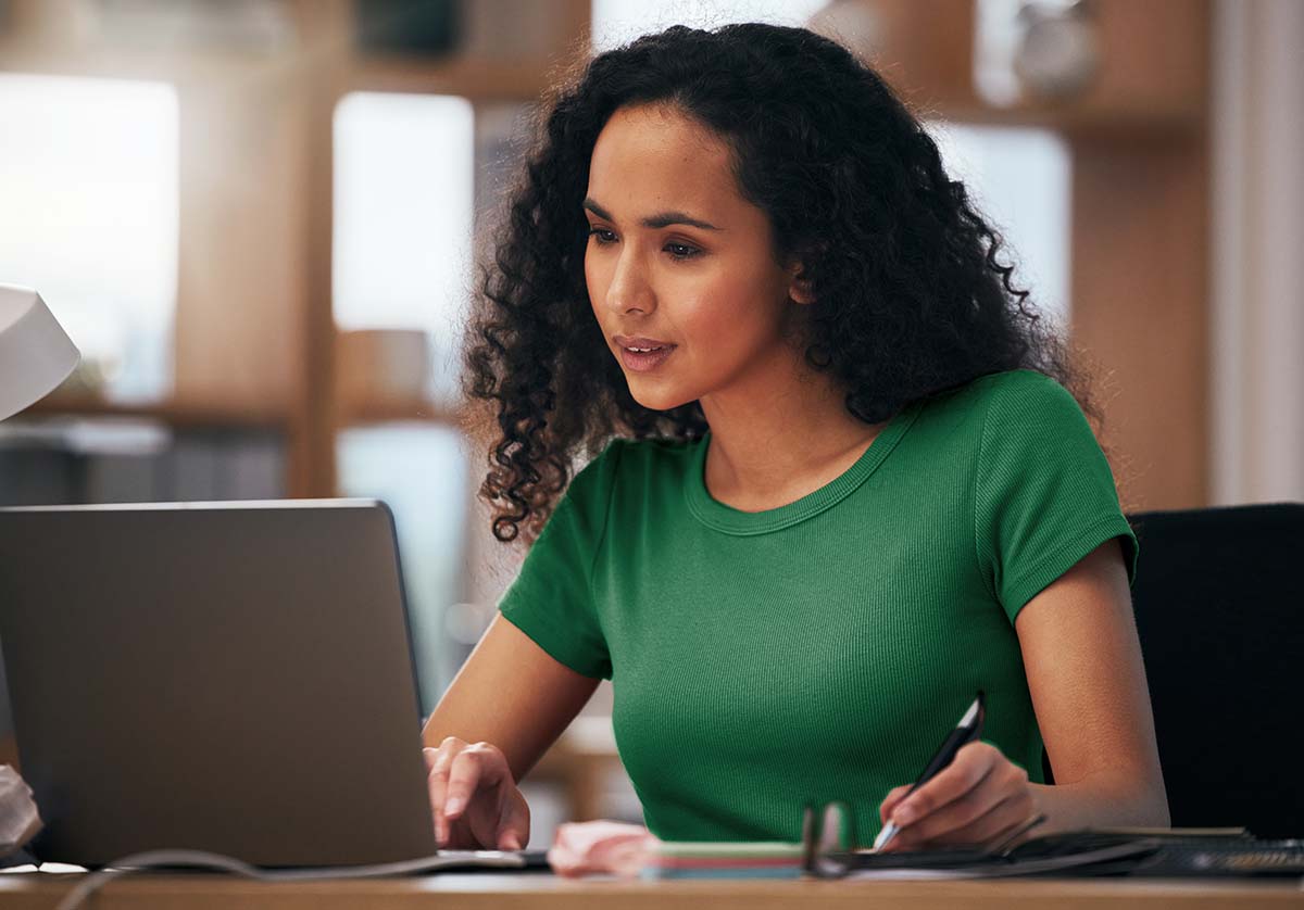 A woman looking intrigued at a laptop with a pen in her left hand