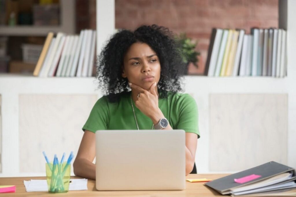 A woman sitting at a desk with laptop pondering