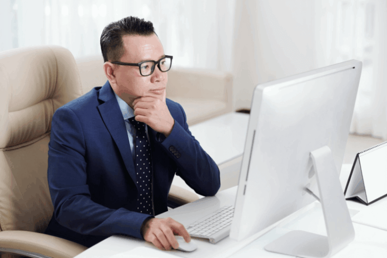 Man wearing glasses sitting at desk looking at desktop monitor