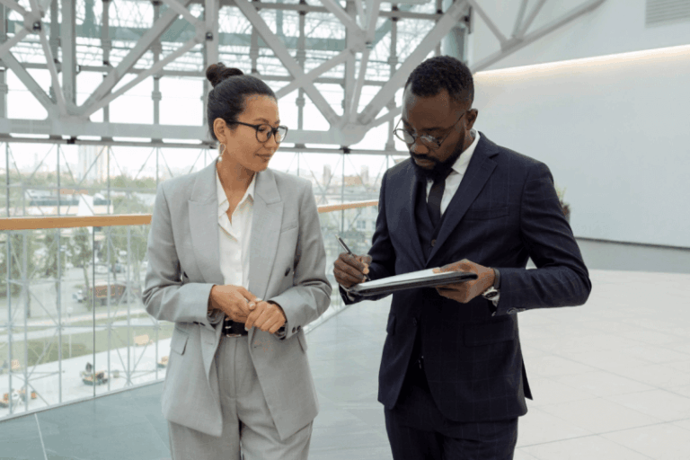 Man in suite writing on note pad while talking to woman in office building
