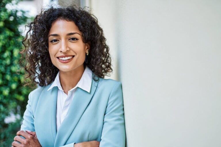 Women with curly hair leaning against wall in business attire