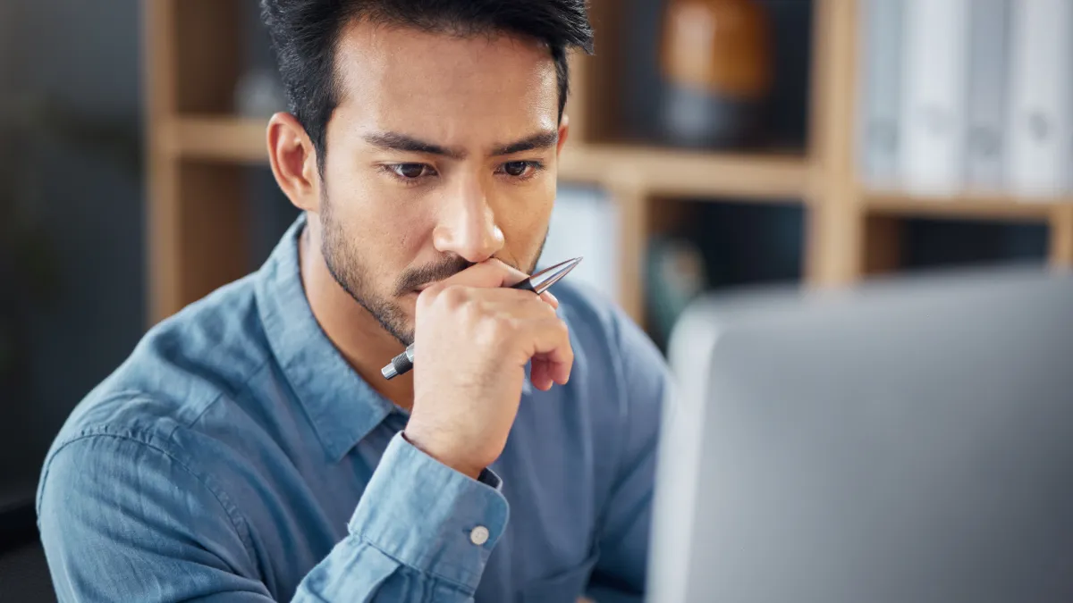 Man holding pen looking at screen in deep thought