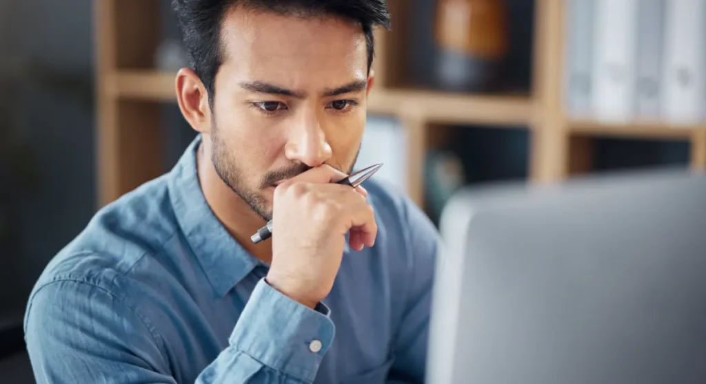 Man holding pen looking at screen in deep thought