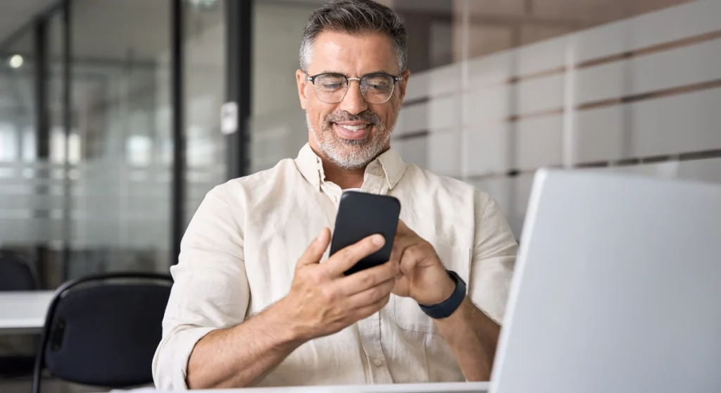 Man looking at phone reading Billtrust blog: Suppliers can’t avoid payment processing costs, but they can control them