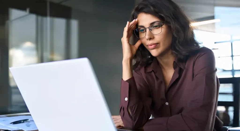 woman wearing glasses looking at laptop thinking deeply