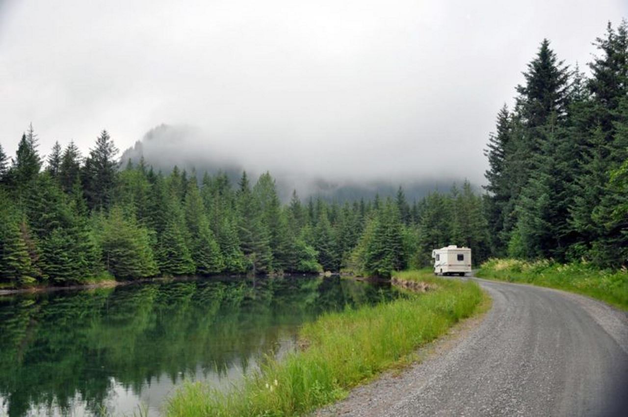 camper driving through forrest next to body of water
